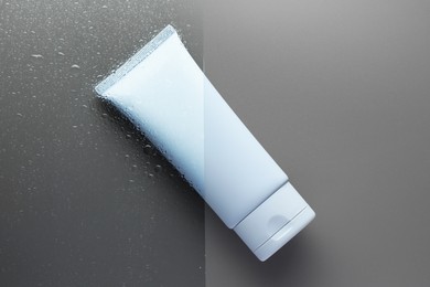 Tube with moisturizing cream on wet grey surface, top view