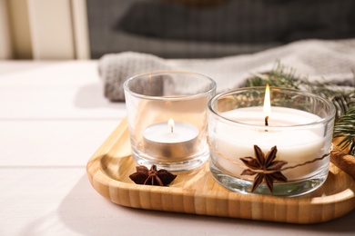 Photo of Wooden tray with decorated scented candles on white table