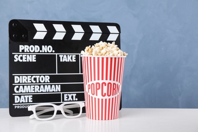 Photo of Delicious popcorn, glasses and clapper on white wooden table. Space for text