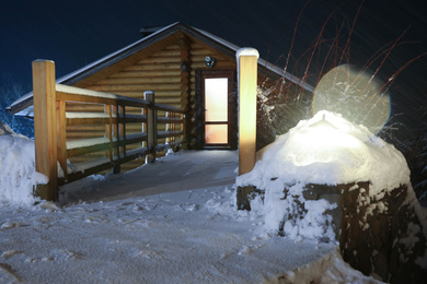 Photo of Bridge covered with snow near wooden cottage at night. Winter vacation