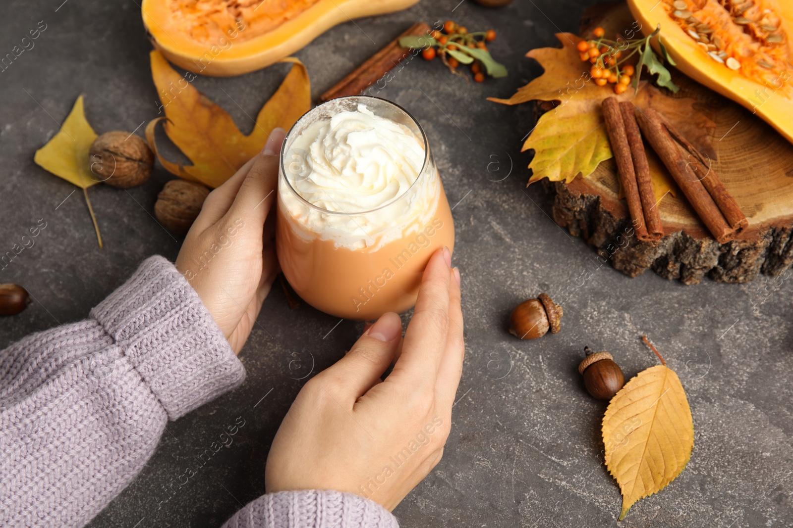 Photo of Woman holding glass with pumpkin spice latte cream on table