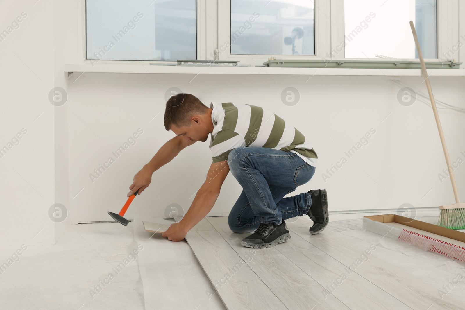 Photo of Professional worker using hammer during installation of new laminate flooring indoors