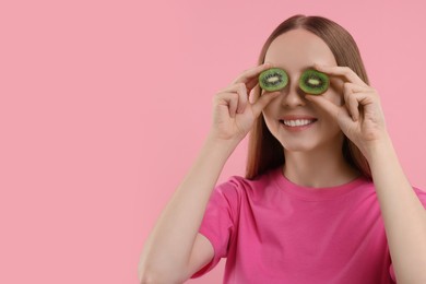 Photo of Young woman holding halves of kiwi near her eyes on pink background. Space for text