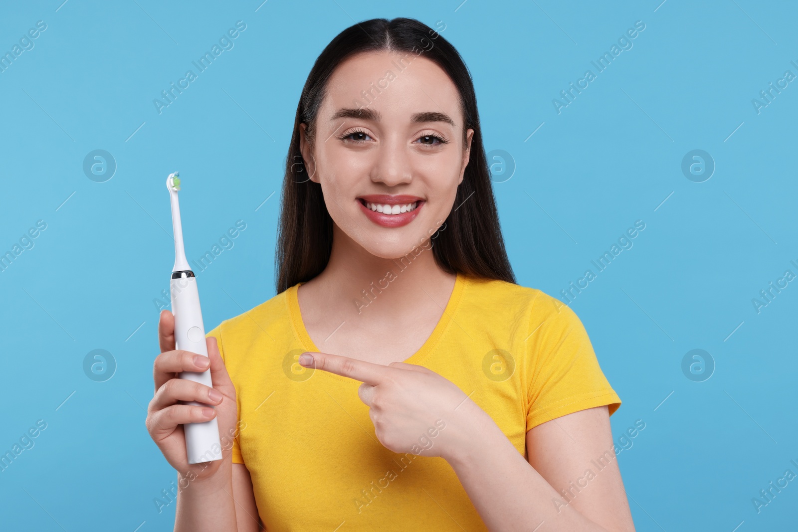 Photo of Happy young woman holding electric toothbrush on light blue background