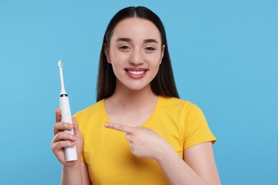 Happy young woman holding electric toothbrush on light blue background