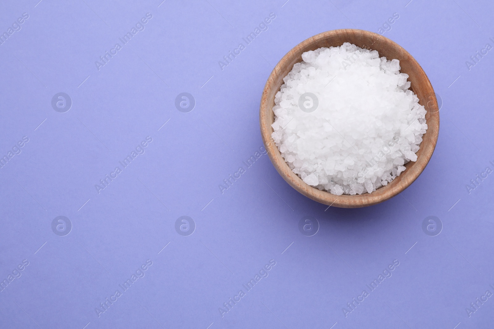 Photo of Bowl of sea salt on violet background, top view. Space for text