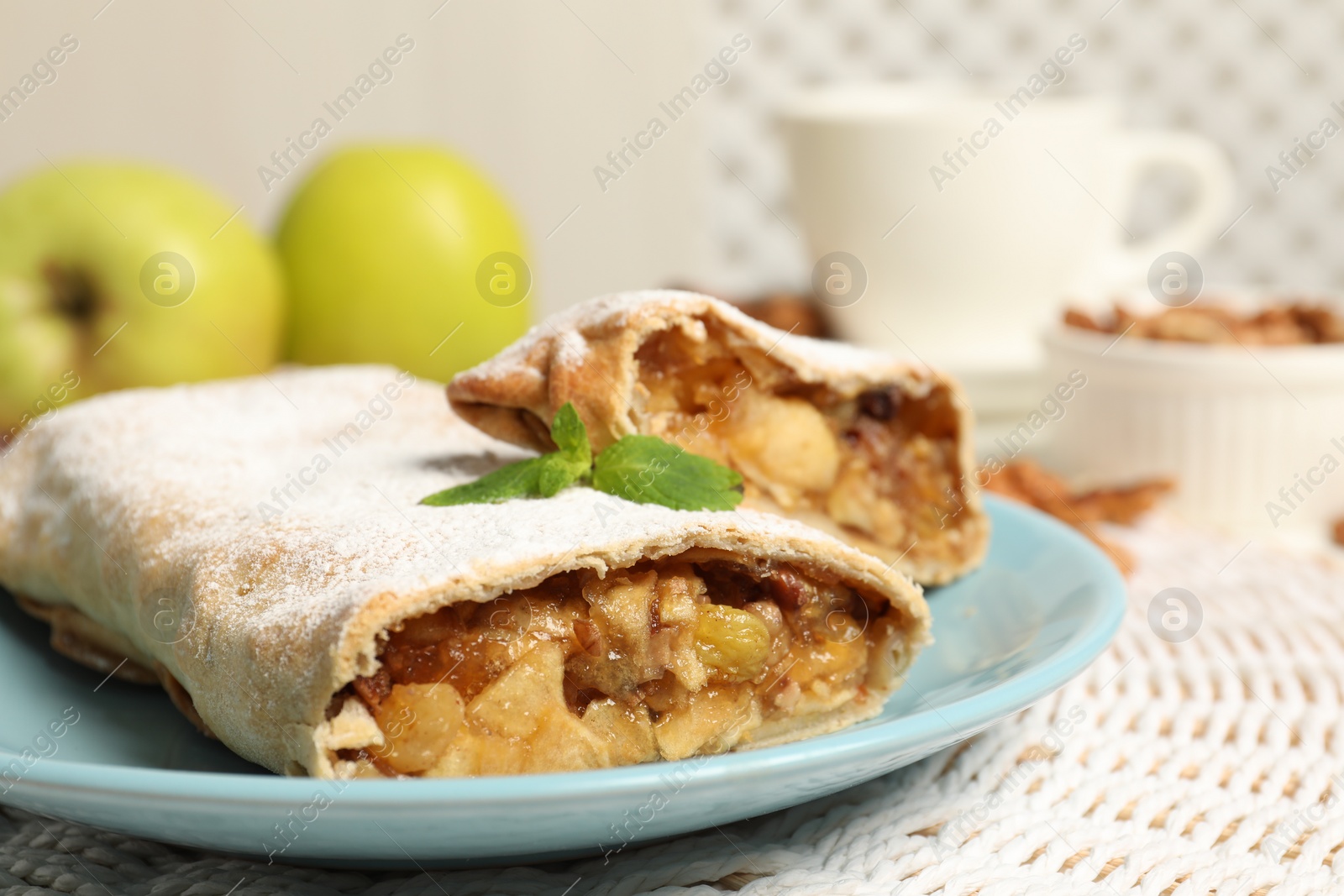 Photo of Delicious strudel with apples, nuts and raisins on wicker mat, closeup