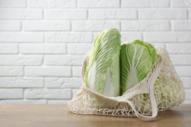 Fresh Chinese cabbages in string bag on wooden table near white brick wall. Space for text