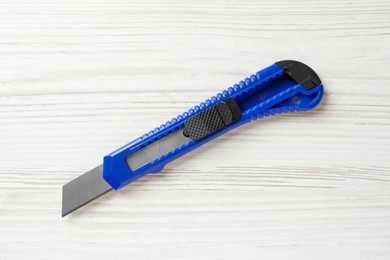 Photo of Blue utility knife on white wooden table, top view. Construction tool