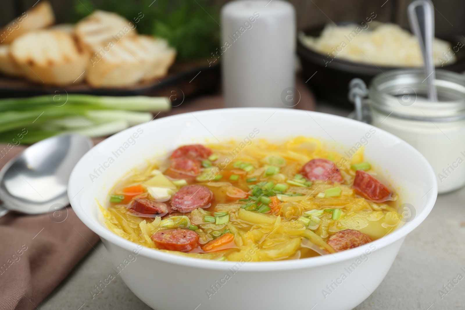 Photo of Delicious sauerkraut soup with smoked sausages and green onion on table, closeup