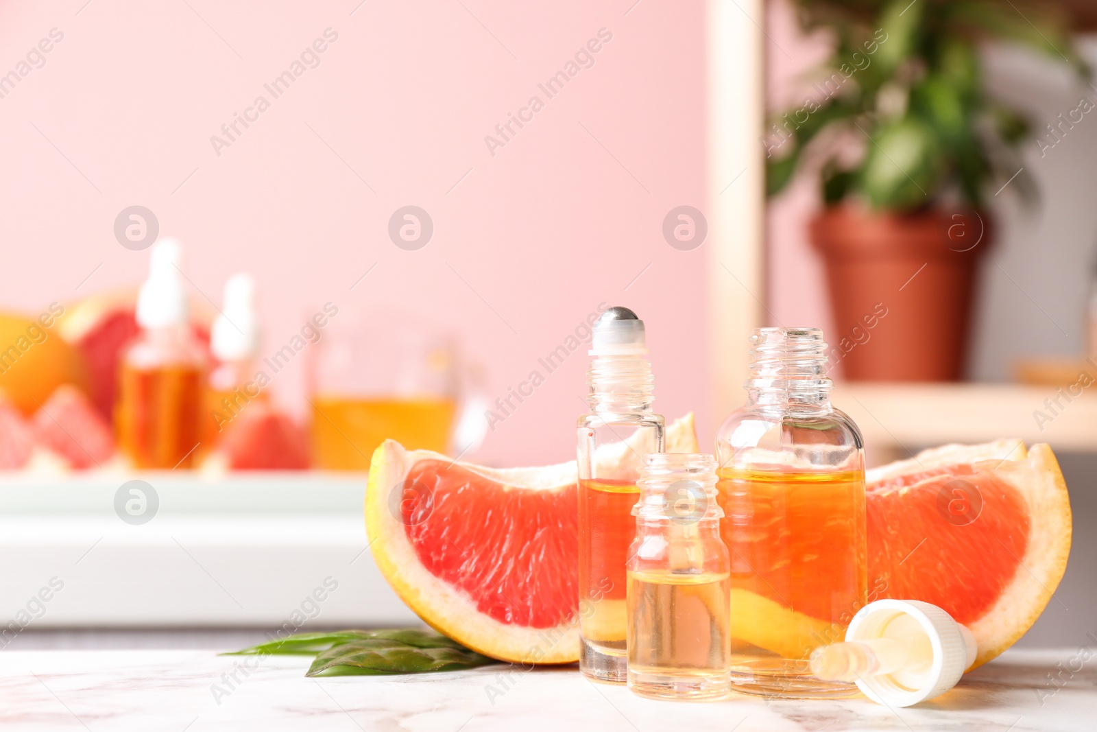 Photo of Bottles of essential oil and grapefruit slices on table against blurred background. Space for text