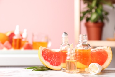 Bottles of essential oil and grapefruit slices on table against blurred background. Space for text