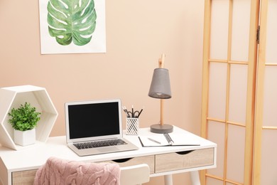 Photo of Cozy workplace with laptop and stationery on desk at home