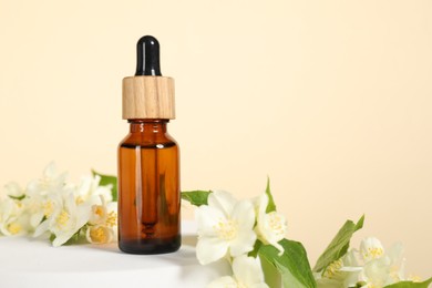 Presentation of essential oil in bottle and beautiful jasmine flowers against beige background, space for text