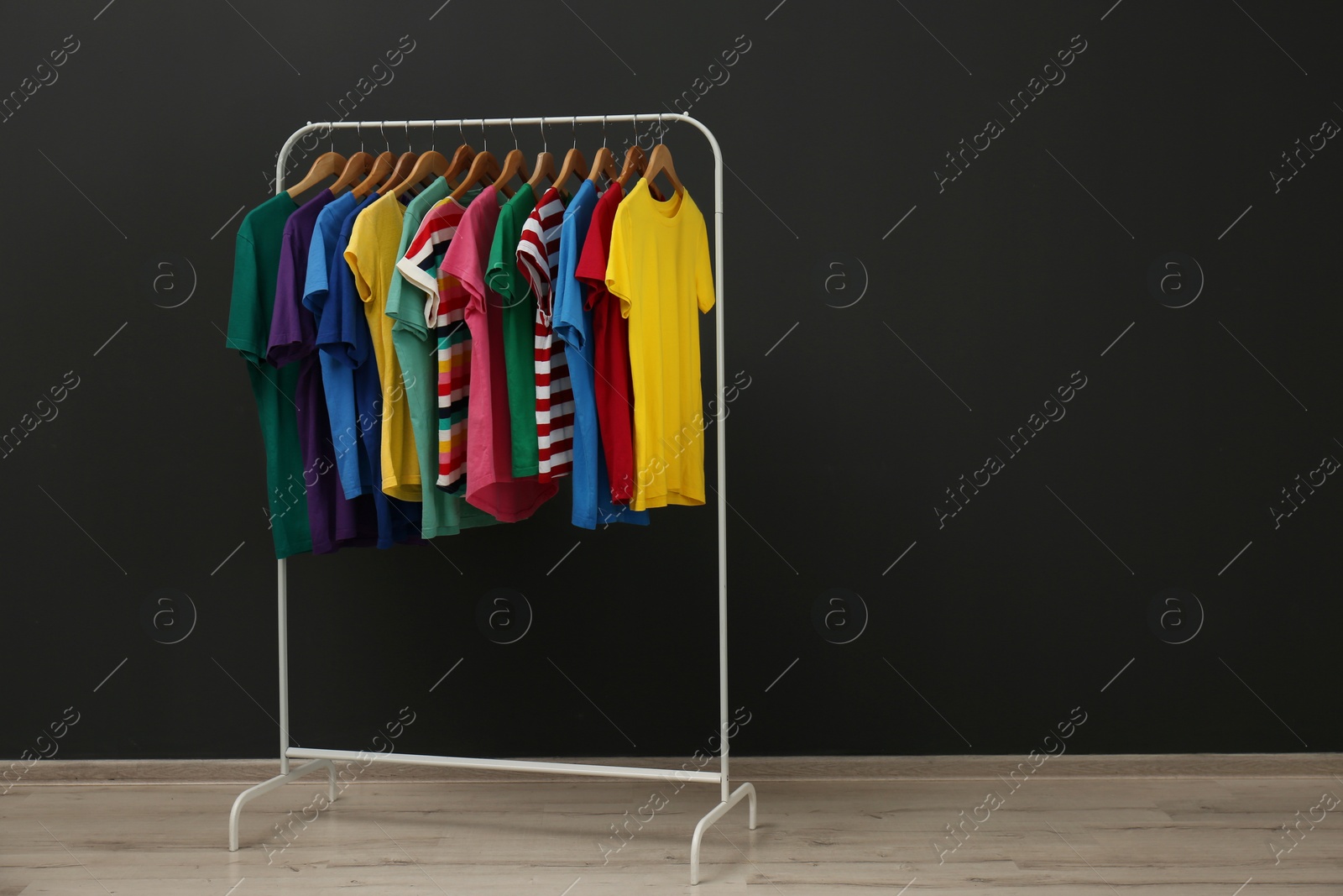 Photo of Rack with stylish clothes near black wall. Space for text