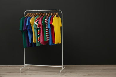 Photo of Rack with stylish clothes near black wall. Space for text