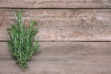 Photo of Sprigs of rosemary on wooden table, top view. Space for text