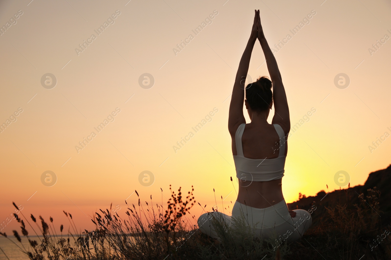 Photo of Woman meditating outdoors at sunset, back view. Space for text