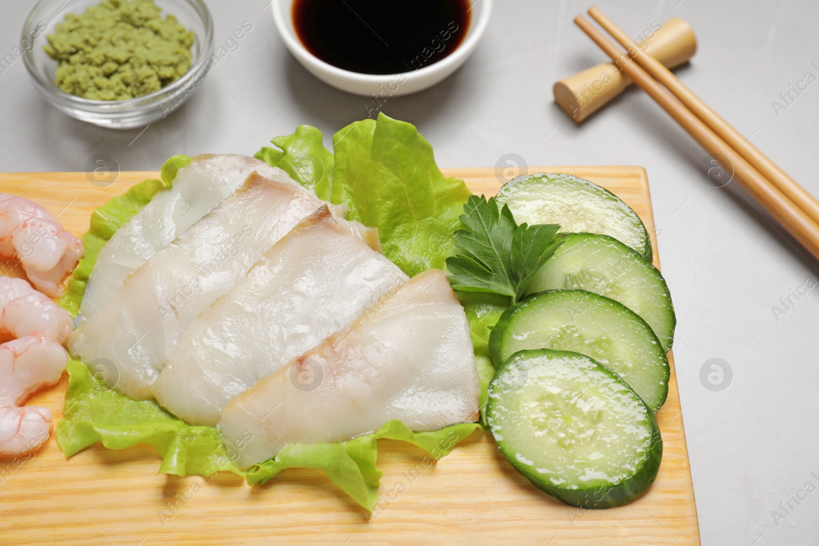 Photo of Sashimi set served with cucumber, lettuce, soy sauce and vasabi on light grey table, closeup