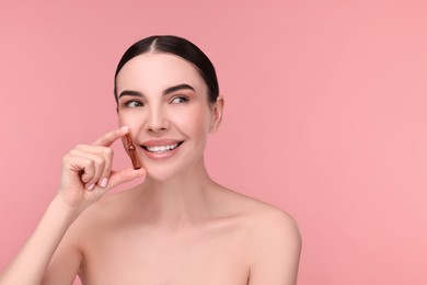 Beautiful young woman holding skincare ampoule on pink background. Space for text