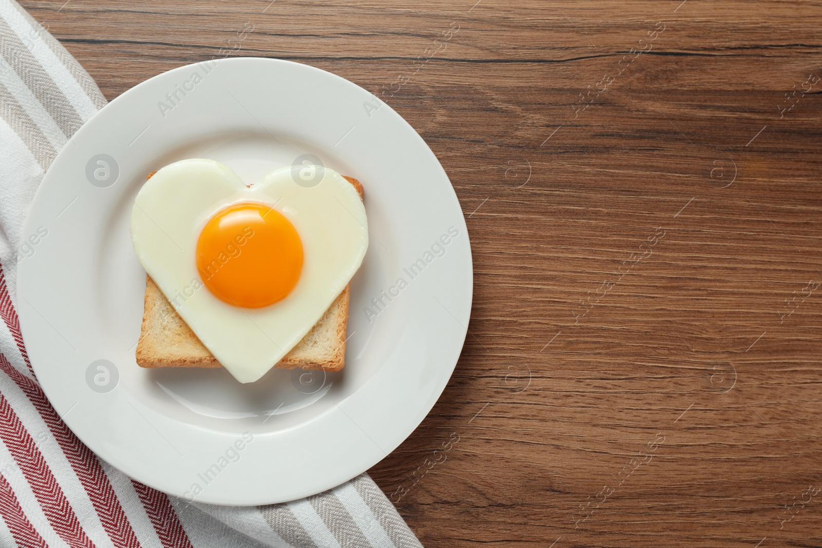 Photo of Plate with heart shaped fried egg and toast on wooden table, top view. Space for text