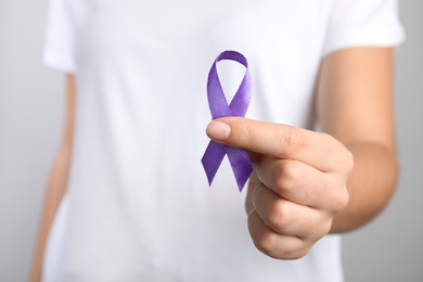 Woman holding purple ribbon on grey background, closeup. Domestic violence awareness