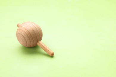 Photo of One wooden spinning top on light green background, space for text. Toy whirligig