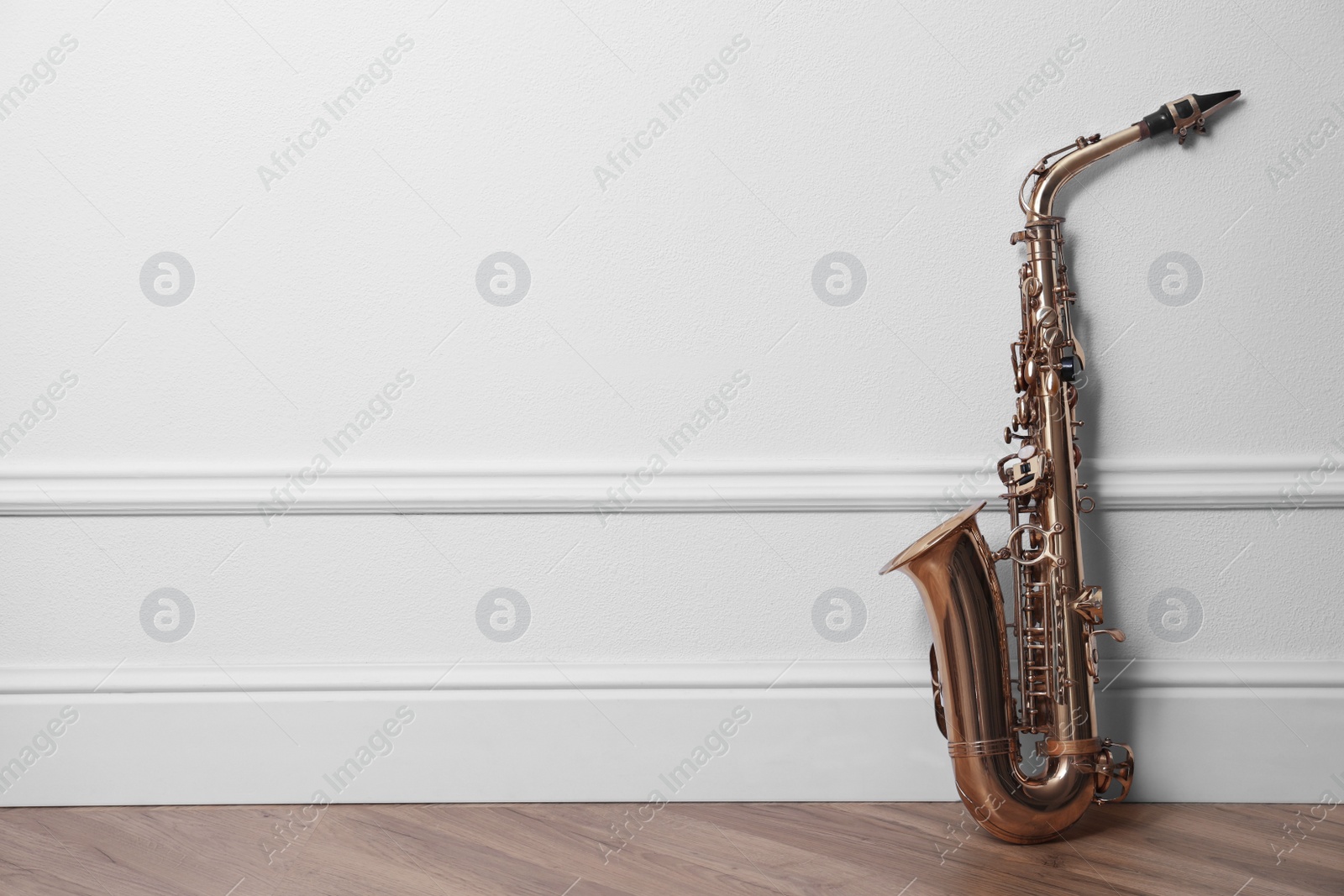 Photo of Beautiful saxophone on floor near white wall indoors, space for text