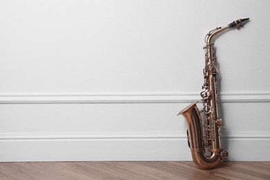 Beautiful saxophone on floor near white wall indoors, space for text