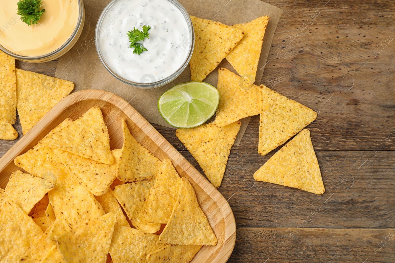 Photo of Mexican nacho chips with different sauces on wooden background, flat lay. Space for text