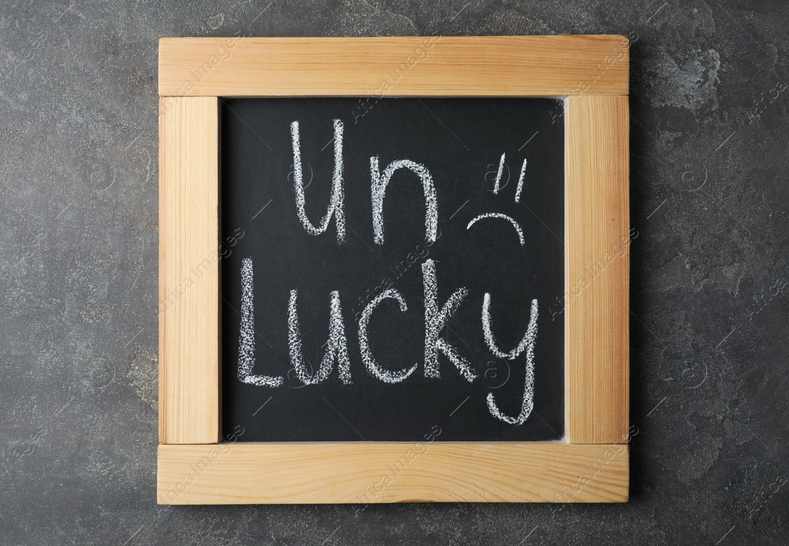 Photo of Blackboard with word UNLUCKY and sad face on grey stone background, top view