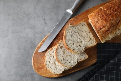 Photo of Freshly baked cut sourdough bread and knife on grey table, top view. Space for text