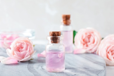 Photo of Bottles with rose essential oil and flowers on stone board