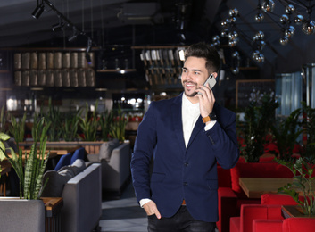 Photo of Young business owner talking on phone in his cafe