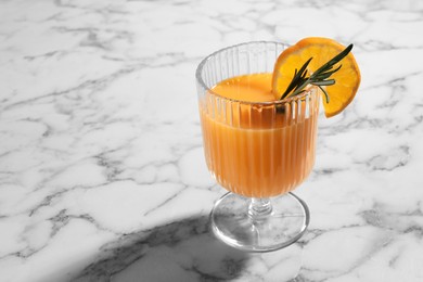 Delicious tangerine liqueur in glass and rosemary on white marble table, closeup. Space for text