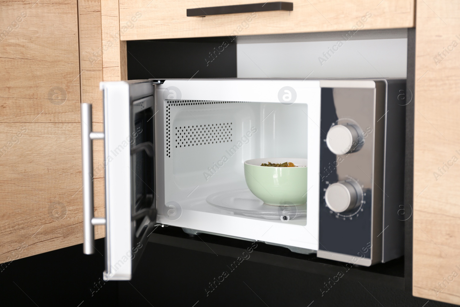 Photo of Open modern microwave oven with dish in kitchen