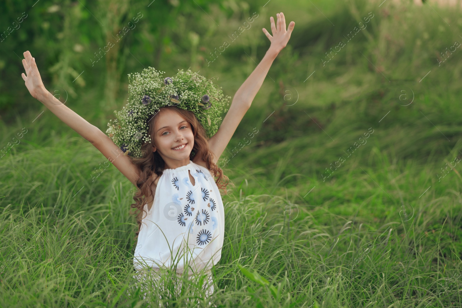 Photo of Cute little girl wearing wreath made of beautiful flowers in field