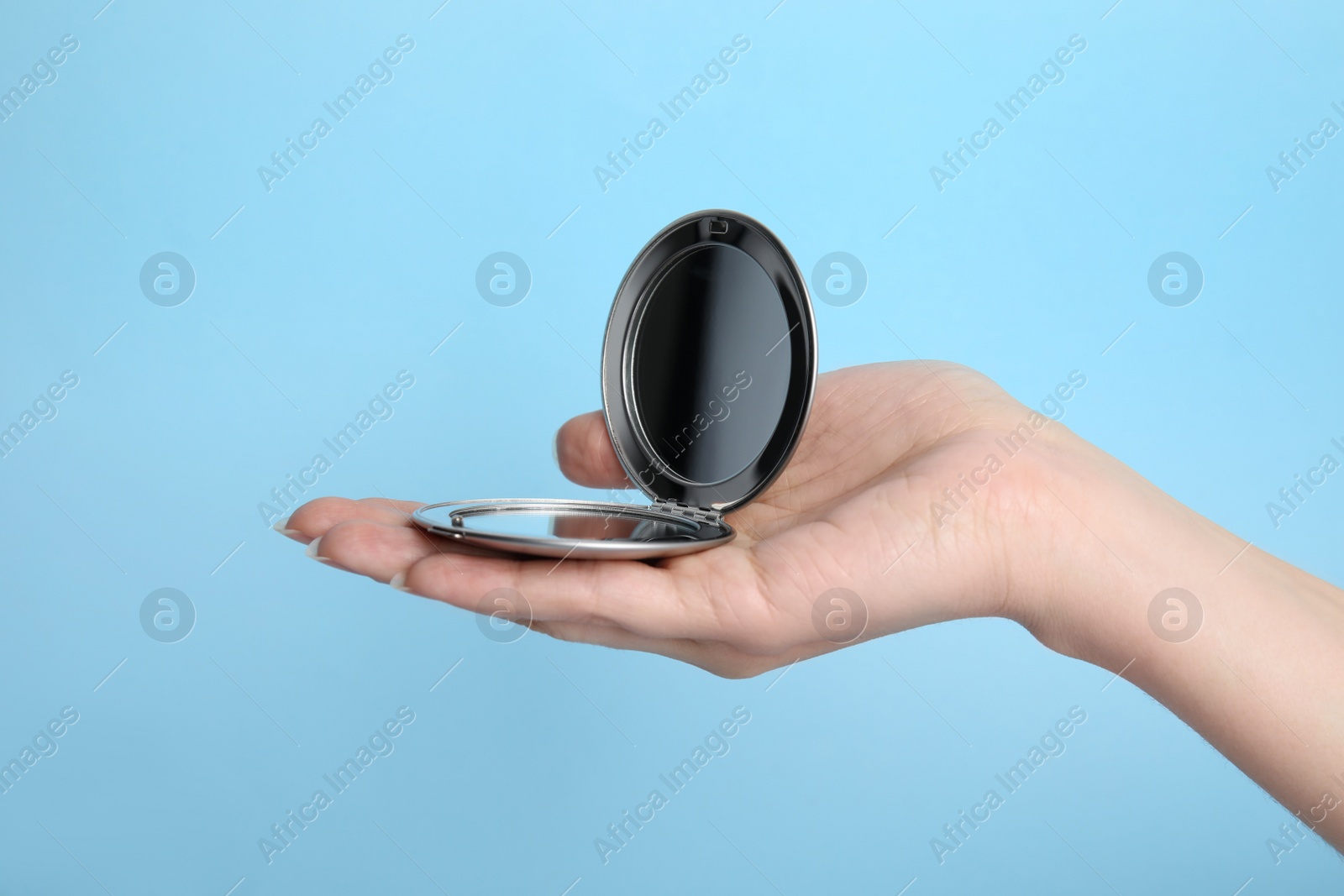 Photo of Woman holding stylish cosmetic pocket mirror on light blue background, closeup