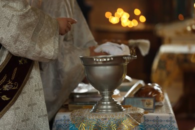 Photo of Priests preparing for baptism ceremony. Silver vessel with holy water on stand in church