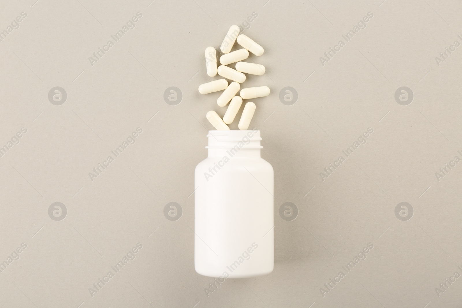 Photo of Bottle and vitamin capsules on light background, top view