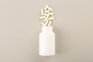 Bottle and vitamin capsules on light background, top view