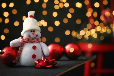 Image of Cute snowman, bow and Christmas balls on table, bokeh effect. Space for text