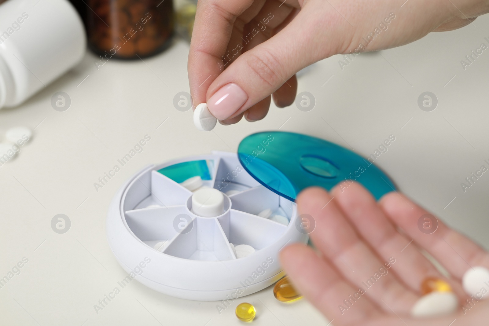 Photo of Woman taking pill from plastic container at white table, closeup