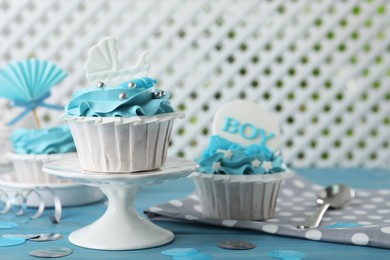 Photo of Delicious cupcakes with light blue cream and toppers for baby shower on table