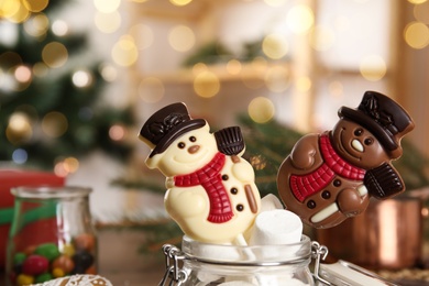 Photo of Funny chocolate snowmen candies in glass jar with marshmallows, closeup