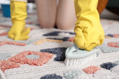 Woman in rubber gloves cleaning carpet with brush indoors, closeup. Space for text