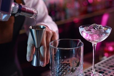 Cocktail making. Bartender pouring alcohol from bottle into jigger in bar, closeup