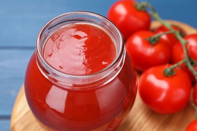 Photo of Organic ketchup in glass jar and fresh tomatoes on table, closeup. Tomato sauce