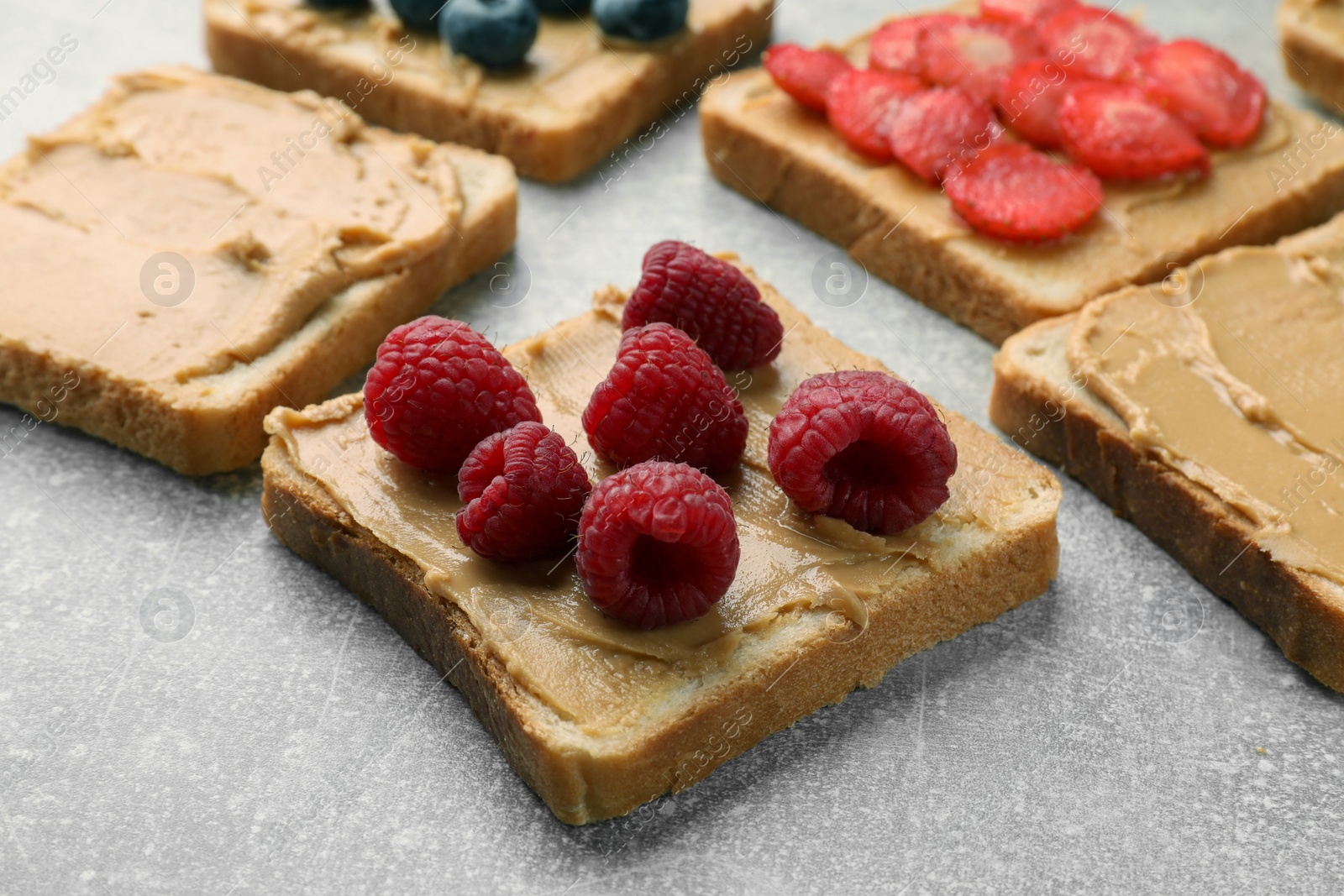 Photo of Tasty peanut butter sandwiches with fresh berries on gray table, closeup