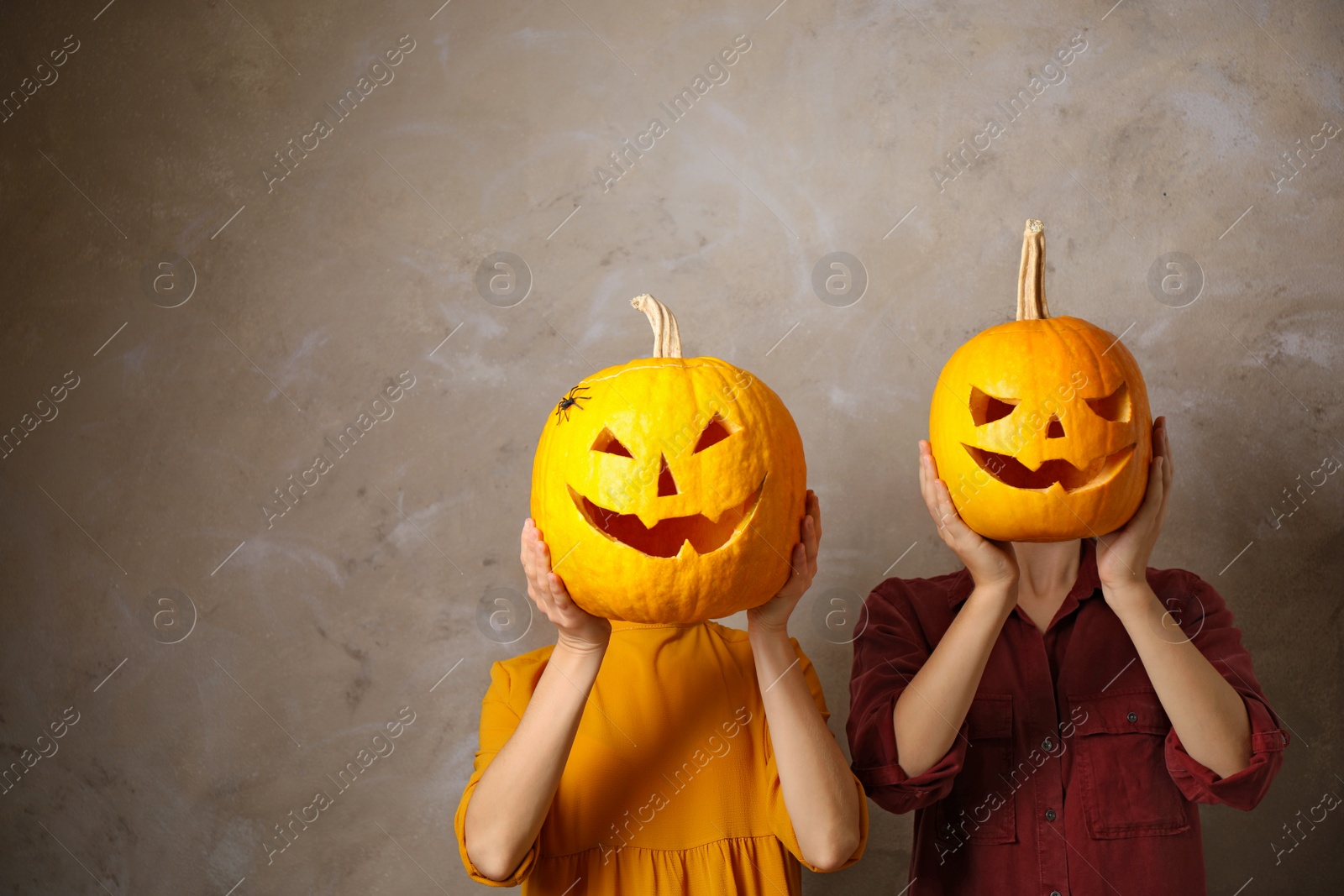 Photo of Women with pumpkin heads against beige background, space for text. Jack lantern - traditional Halloween decor